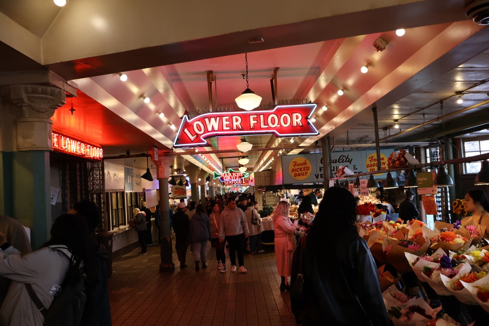 Neon Lower Floor sign inside Pike Place Market with flower vendors